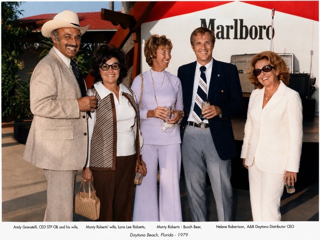 Group photo at Daytona Beach in 1979: Andy Granatelli and wife, Lora Lee Roberts, Monty Roberts of Busch Beer, and Helene Robertson, with a Marlboro backdrop